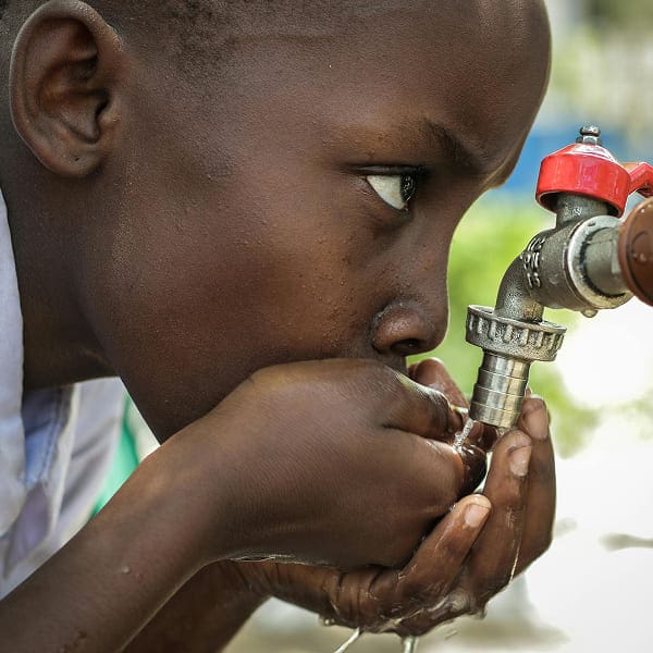 A child drinks water using cupped hands from an outdoor faucet, reflecting one of our causes: ensuring access to clean water for every child.