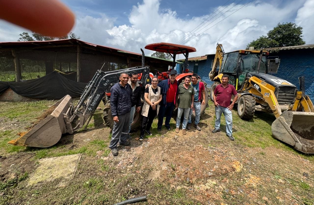 Seven people stand in front of two tractors on a grassy area, posing for a group photo outdoors as they support our causes. One person’s finger partially covers the camera lens in the top left corner.